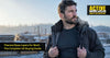 Tradesperson holding open a work jacket to show a fitted thermal base layer underneath, on a frosty UK building site with breath visible in the cold air